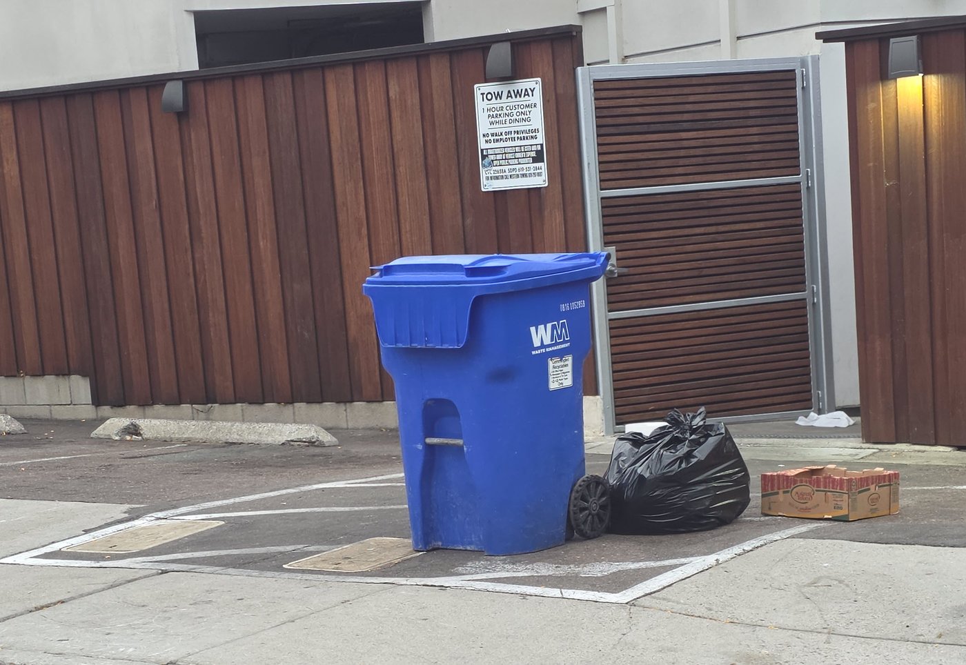 July 9, 2026, 6:29 a.m.: a recycling bin, a trash bag, and a produce box left out by the enclosure.